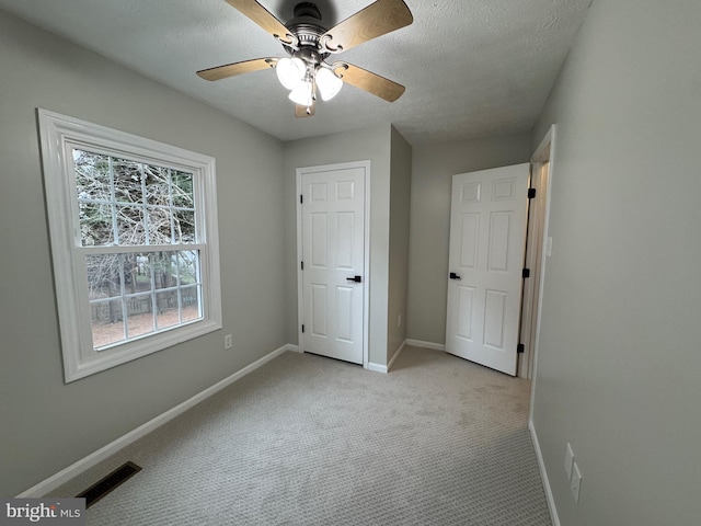 unfurnished bedroom featuring ceiling fan, light colored carpet, and a textured ceiling