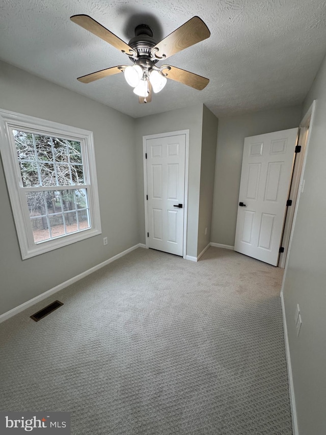 unfurnished bedroom featuring ceiling fan, light colored carpet, and a textured ceiling