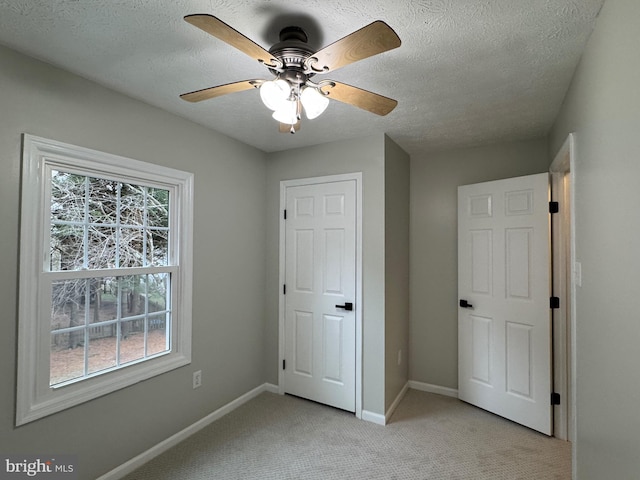 unfurnished bedroom featuring ceiling fan, light colored carpet, and a textured ceiling