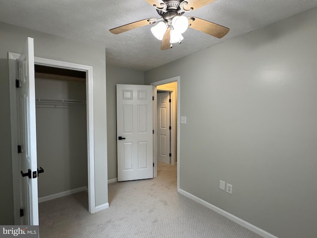 unfurnished bedroom featuring light carpet, a textured ceiling, a closet, and ceiling fan