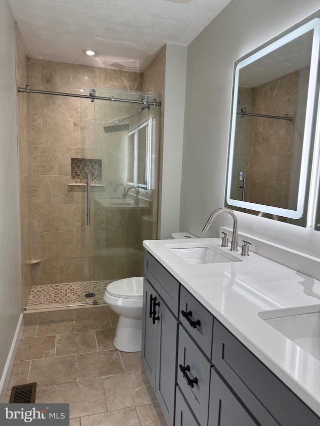 bathroom with vanity, a textured ceiling, tiled shower, and toilet