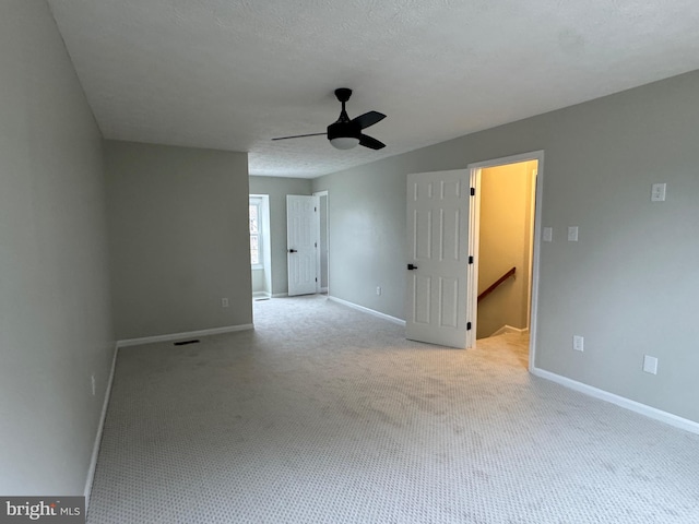 empty room featuring a textured ceiling, light colored carpet, and ceiling fan