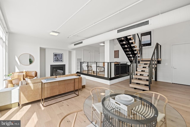 living area featuring visible vents, light wood-style flooring, stairs, and a glass covered fireplace