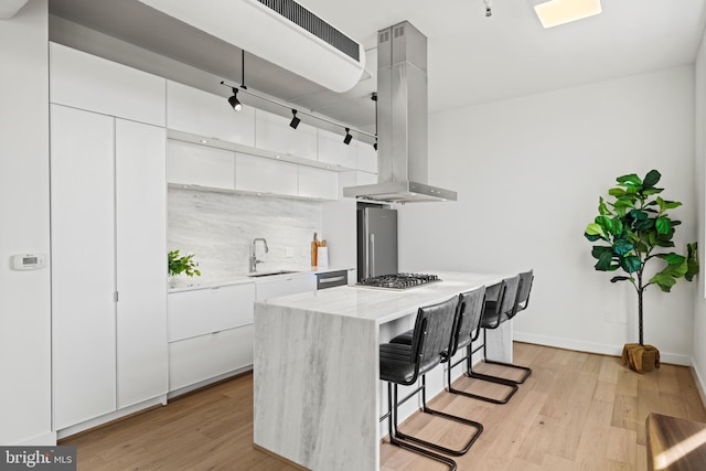 kitchen featuring a center island, a kitchen bar, appliances with stainless steel finishes, island exhaust hood, and a sink