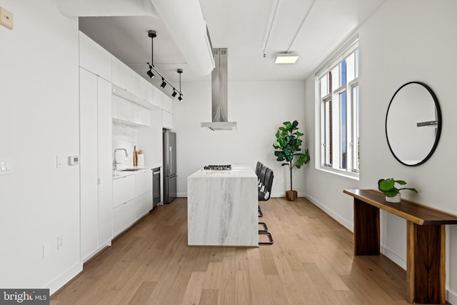 kitchen with a sink, light countertops, appliances with stainless steel finishes, wall chimney exhaust hood, and modern cabinets