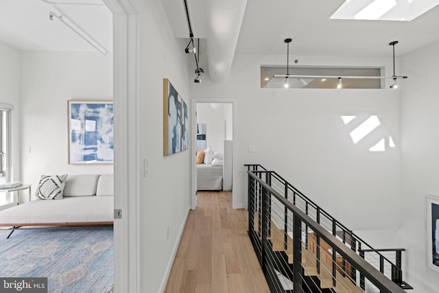 corridor featuring a skylight, an upstairs landing, baseboards, and light wood finished floors