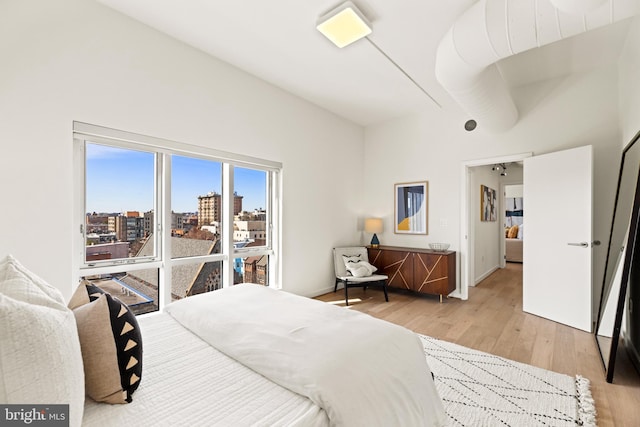 bedroom with a view of city and light wood finished floors