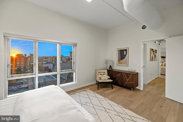 bedroom featuring baseboards, a view of city, and light wood-style floors