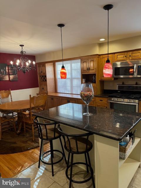 kitchen featuring pendant lighting, an inviting chandelier, light hardwood / wood-style flooring, appliances with stainless steel finishes, and a breakfast bar area