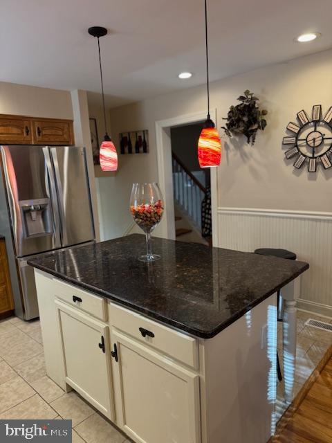 kitchen with stainless steel fridge with ice dispenser, hanging light fixtures, and dark stone counters