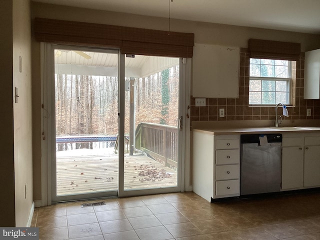 kitchen with tasteful backsplash, stainless steel dishwasher, sink, white cabinets, and light tile patterned flooring