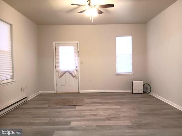 empty room featuring baseboard heating, ceiling fan, and dark hardwood / wood-style flooring