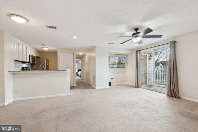 unfurnished living room with ceiling fan, light colored carpet, and a textured ceiling