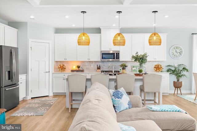 kitchen featuring a kitchen island with sink, decorative light fixtures, white cabinets, and appliances with stainless steel finishes