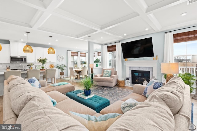 living room with coffered ceiling, a healthy amount of sunlight, a premium fireplace, and light wood-type flooring