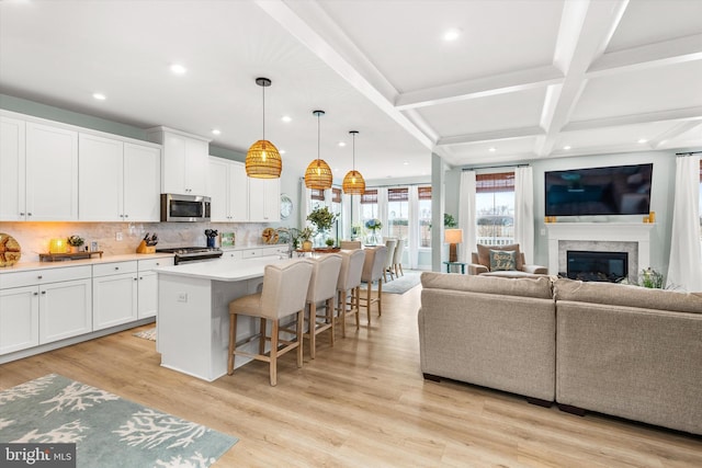 kitchen featuring appliances with stainless steel finishes, pendant lighting, white cabinets, a kitchen breakfast bar, and a kitchen island with sink