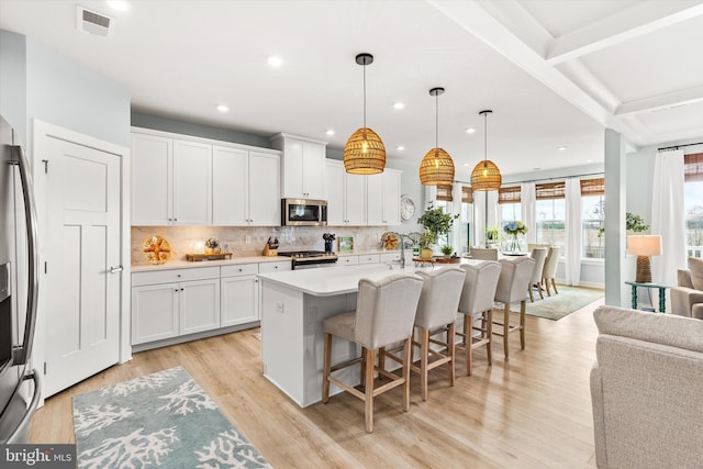 kitchen with a breakfast bar, decorative light fixtures, a center island with sink, appliances with stainless steel finishes, and white cabinets