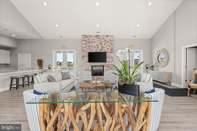 living room featuring french doors, sink, high vaulted ceiling, a brick fireplace, and light hardwood / wood-style flooring