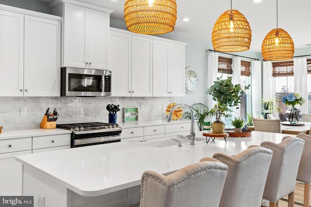 kitchen featuring sink, a kitchen island with sink, hanging light fixtures, white cabinetry, and stainless steel appliances