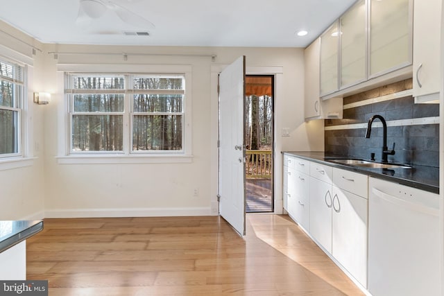 kitchen with white dishwasher, sink, light wood-type flooring, tasteful backsplash, and white cabinetry