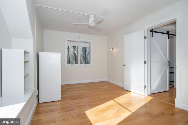 spare room with a barn door, light hardwood / wood-style floors, and ceiling fan