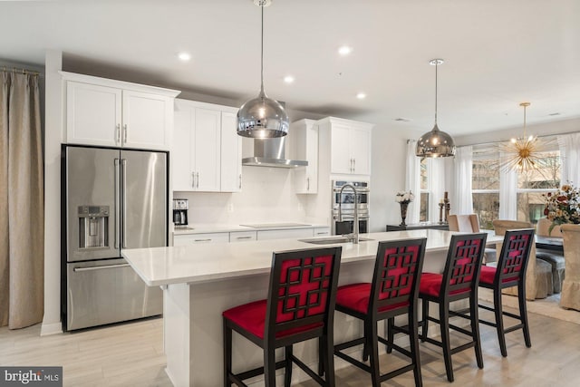 kitchen featuring appliances with stainless steel finishes, light hardwood / wood-style flooring, white cabinets, a breakfast bar area, and an island with sink