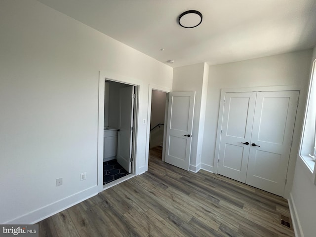 unfurnished bedroom with ensuite bathroom, dark wood-type flooring, and a closet