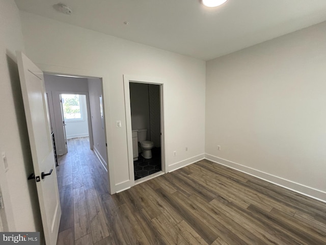 unfurnished bedroom with connected bathroom and dark wood-type flooring