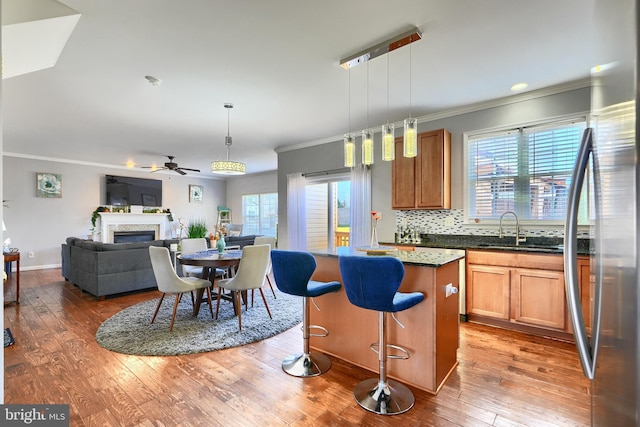 kitchen with stainless steel refrigerator, ceiling fan, sink, hanging light fixtures, and a kitchen island