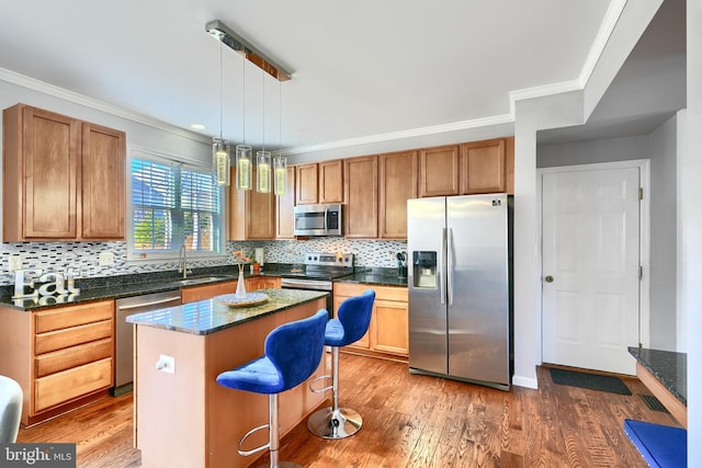 kitchen with hanging light fixtures, appliances with stainless steel finishes, a kitchen island, a kitchen bar, and wood-type flooring