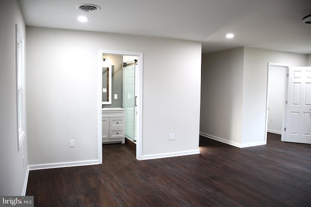 interior space featuring a barn door, ensuite bathroom, and dark wood-type flooring