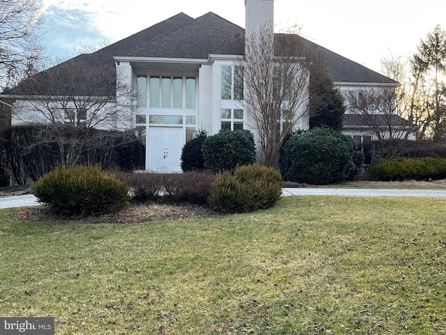 exterior space featuring brick siding, a chimney, and a front yard