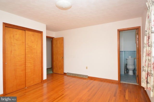 unfurnished bedroom featuring ensuite bath, a closet, wood-type flooring, and tile walls