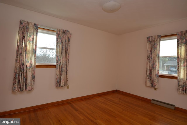 unfurnished room with plenty of natural light, wood-type flooring, and baseboard heating