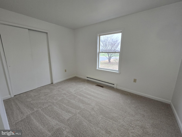 unfurnished bedroom with a closet, light colored carpet, and a baseboard heating unit