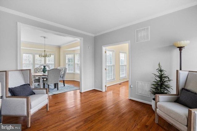 living area with crown molding, hardwood / wood-style floors, and an inviting chandelier