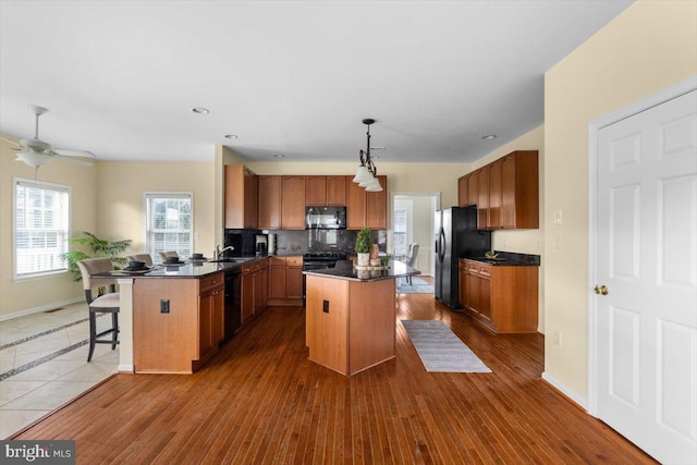 kitchen with hanging light fixtures, black appliances, kitchen peninsula, and a kitchen island