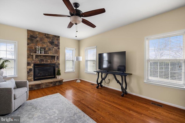 living room with hardwood / wood-style floors, a stone fireplace, and ceiling fan