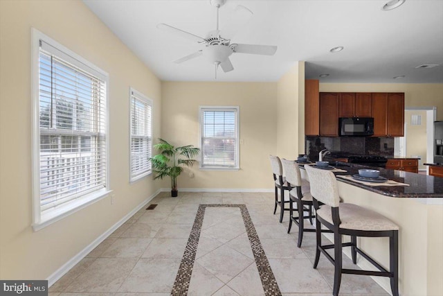 kitchen featuring light tile patterned floors, stainless steel fridge, a kitchen breakfast bar, ceiling fan, and decorative backsplash