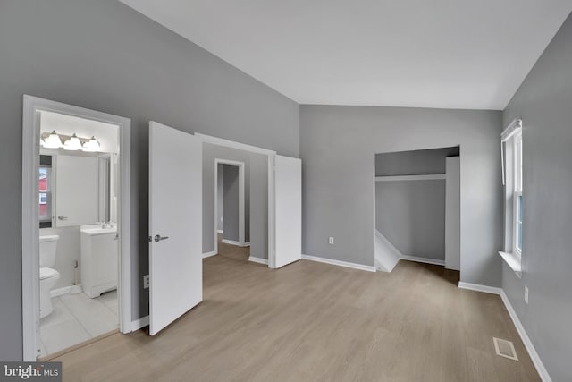 unfurnished bedroom with ensuite bath, sink, light hardwood / wood-style floors, and vaulted ceiling