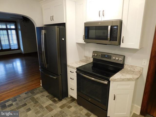 kitchen with light stone counters, white cabinetry, stainless steel appliances, and dark hardwood / wood-style floors