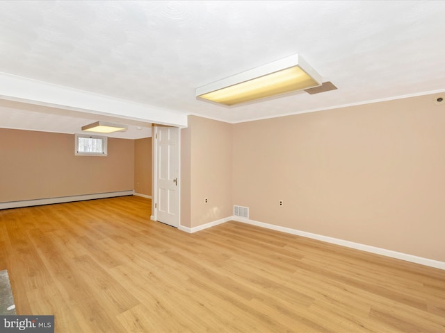 basement with light wood-type flooring, ornamental molding, and a baseboard radiator