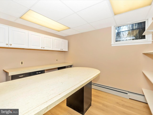 kitchen with a paneled ceiling, white cabinetry, baseboard heating, and light hardwood / wood-style flooring