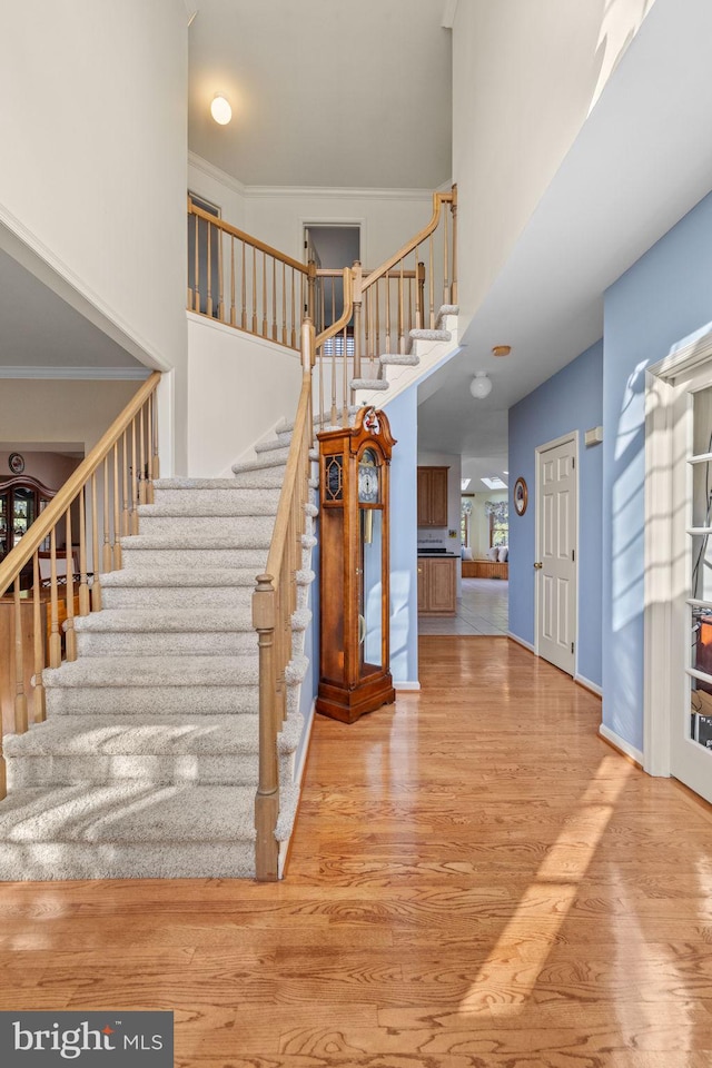 staircase featuring hardwood / wood-style flooring, ornamental molding, and a towering ceiling