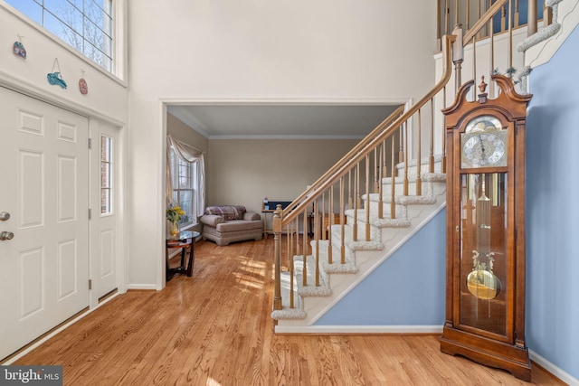 entrance foyer featuring wood-type flooring, a towering ceiling, and ornamental molding