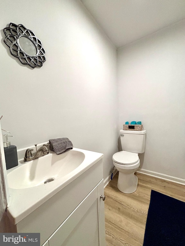 half bathroom with toilet, baseboards, wood finished floors, and vanity