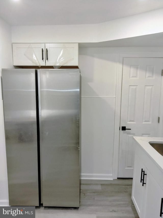 kitchen with stainless steel fridge, white cabinets, and light wood-type flooring