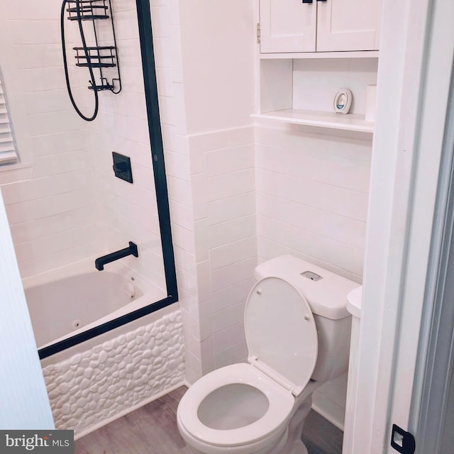 bathroom with tile walls, hardwood / wood-style flooring, tiled shower / bath combo, and toilet