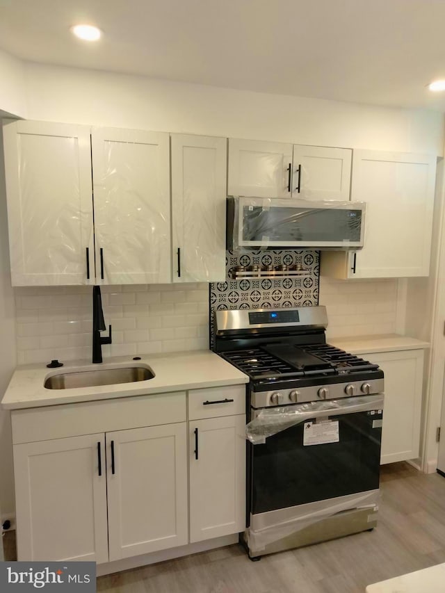 kitchen featuring sink, stainless steel gas range oven, white cabinets, and light wood-type flooring