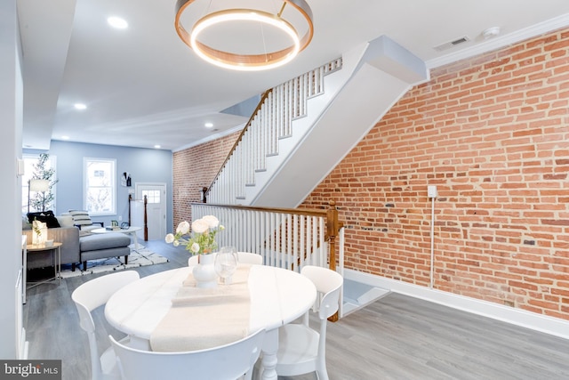 dining room with wood-type flooring, ornamental molding, and brick wall